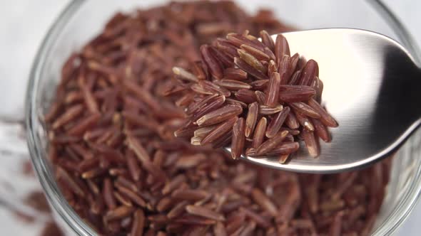 Brown rice falls from a spoon into a glass bowl