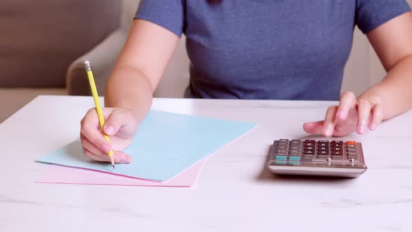 Woman is using a calculator to calculate her monthly expenses and write down her monthly accounting