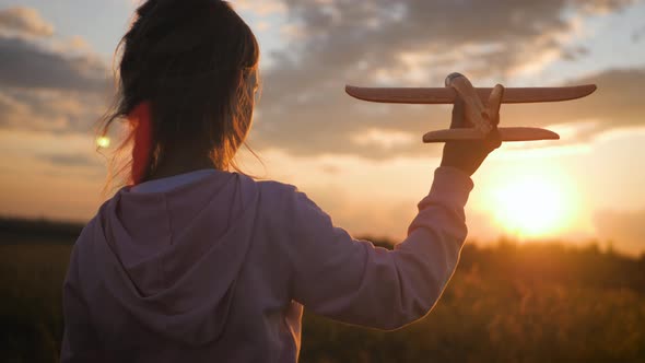 Cute Girl Playing with Toy Airplane in the Wheat Field at Sunset. Silhouette of Child Playing with