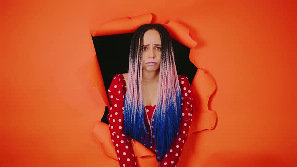 Young Woman with Sad Expression on Her Face Sticking Out of Hole of Orange Background