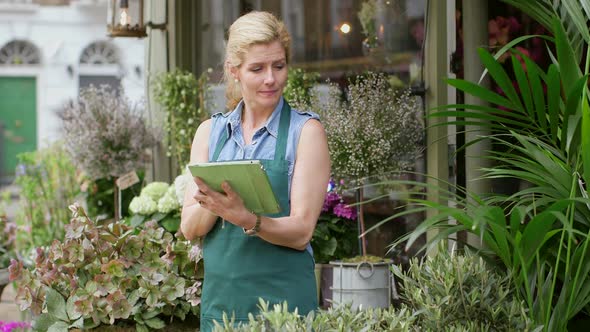 A Florist stands in the doorway of her shop typing into her digital tablet