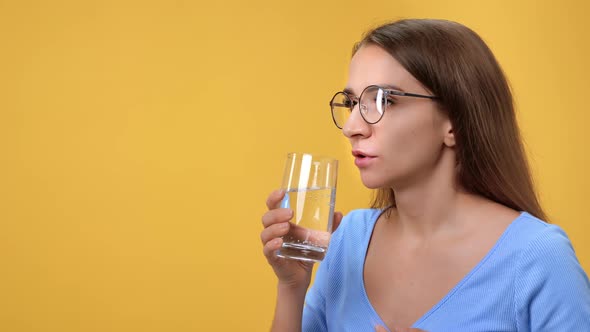 Unwell Young Woman Drinking Medical Pill Vitamin Antibiotic with Water Glass Isolated on Orange