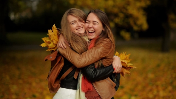 Two Beautiful Teenage Girls Hugging And Holding a Bouquet Of Yellow Leaves In The Autumn Park