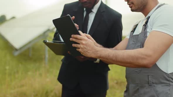 Indian Technician with Digital Tablet in Hands Showing Solar Plant to African