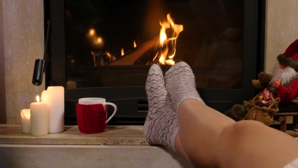 Woman Is Sitting With Cup Of Hot Drink And Book Near The Fireplace