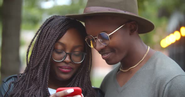 Medium Shot of Cheerful Black Couple Looking at Mobile Phone Outdoors