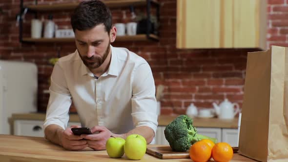 Man Browsing on Mobile Phone at Home Kitchen. Handsome Young Man Browsing on Smartphone Smiling