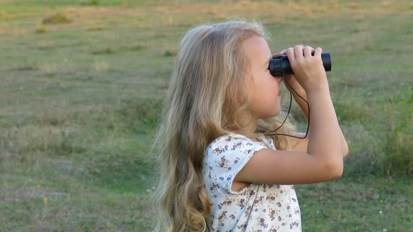 Beautiful Small Girl Looking Through Binoculars. Little Girl On The Lawn Smiles In Camera