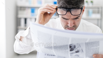 ws on a financial newspaper, he is shocked and adjusting his glasses