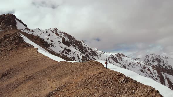 Climber Climbs Uphill with a Backpack and Trekking Sticks on the Ridge at the Junction of Stone and