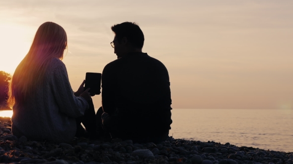 Asian Man And Caucasian Woman Use Tablet Resting On The Sea And Sunset Background