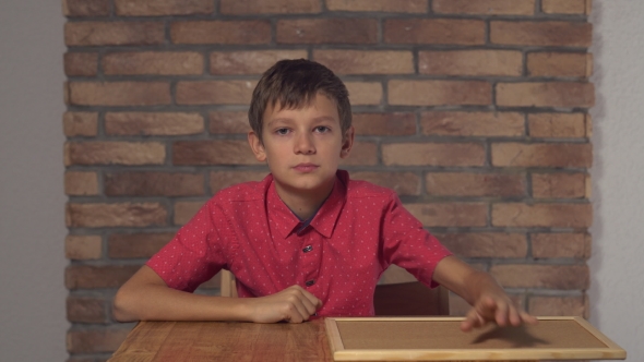 Child Sitting At The Desk Holding Flipchart With Lettering Smile On The Background Red Brick Wall.