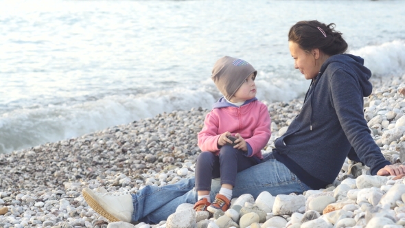 Mother And Child Sit On The Beach And Enjoy The Sunset