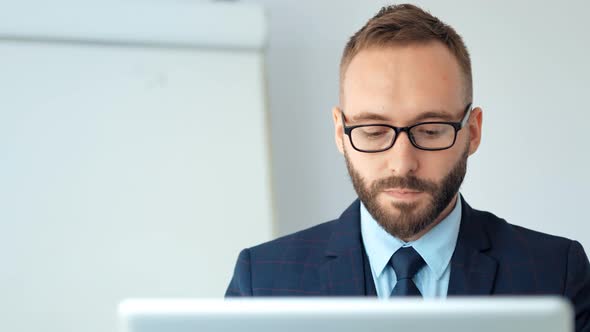 Attractive Businessman in Suit and Glasses Working with Laptop in White Office