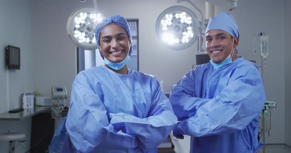 Portrait of diverse male and female surgeon wearing lowered face masks smiling in operating theatre