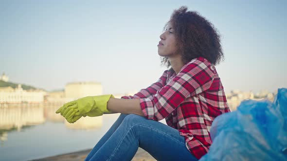 African American Woman Sits on Beach Taking Off Gloves