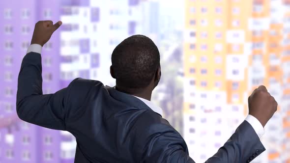 African Man in Suit Rejoises Victory in Skyscrapper, Back View.