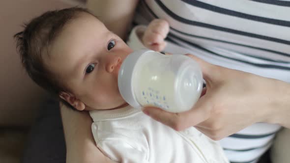 Baby is sucking milk from a bottle in his mother's arms (close-up)