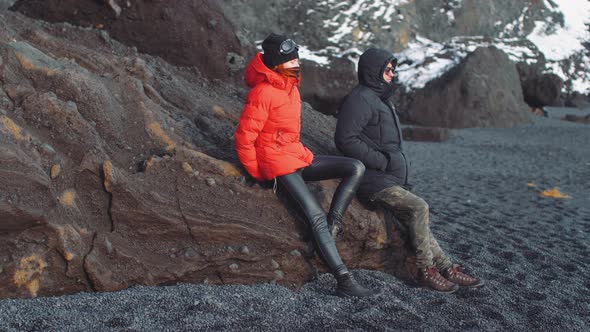 Happy Young Couple Sitting on Big Stone on the Black Volcanic Beach Reynisfjara Iceland