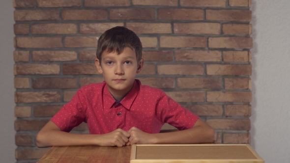 Child Sitting at the Desk Holding Flipchart with Lettering Ok on the Background Red Brick Wall.