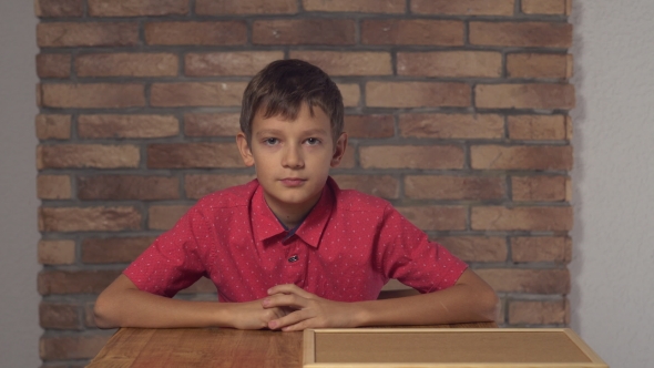 Child Sitting at the Desk Holding Flipchart with Lettering Boss on the Background Red Brick Wall.