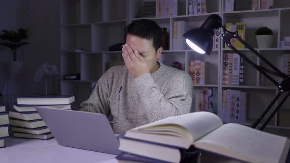 Serious man working on laptop at night, determining information with stressed face on working table