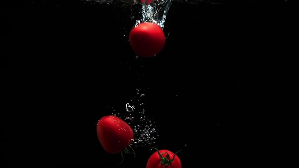 Fresh Ripe Tomatoes Falling Into Clean Water With Air Bubbles And Droplets On Black Background