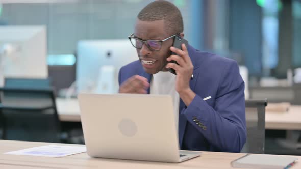 Angry African Businessman Talking on Smartphone in Office