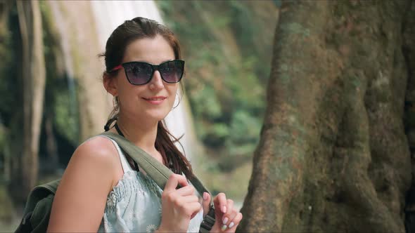 Happy Woman Tourist on Vacation Posing in Front of Waterfalls in Tropical Park