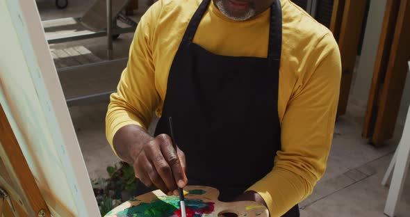 African american senior man standing on a terrace and painting