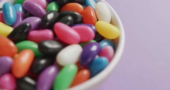 Video of close up of multi coloured sweets in bowl over purple background