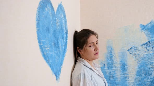 Depressed Brunette Cries Standing Near Wall with Blue Heart