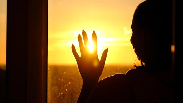 Silhouette Woman at Window Putting Hand to Glass Through Sunset Rays Slow Motion