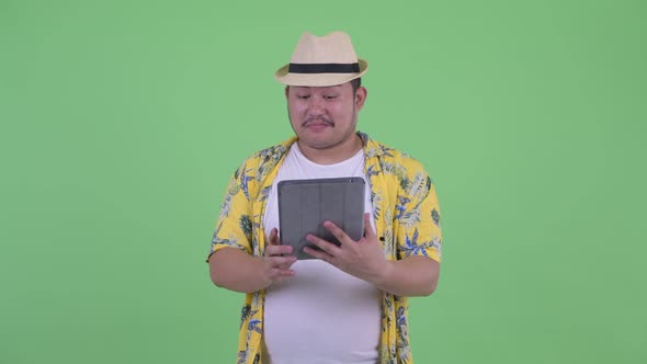 Happy Young Overweight Asian Tourist Man Thinking While Using Digital Tablet