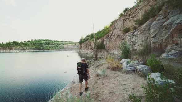 Tourist with a Backpack is Going Along the Bank of the River