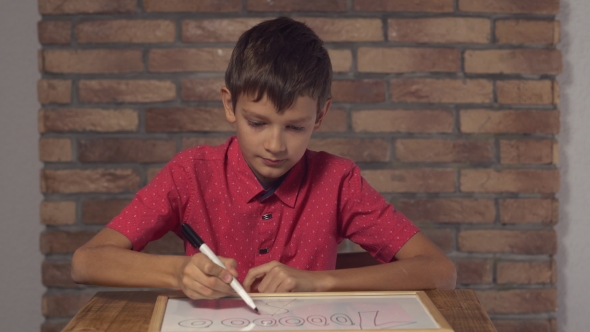 Child Sitting at the Desk Holding Flipchart with Lettering Million on the Background Red Brick Wall.