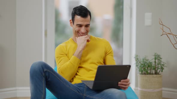 Relaxed Cheerful Middle Eastern Man Laughing Watching Movie on Tablet at Home