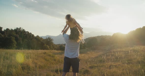 Man Holding Girl in Hands Above Himself and Spinning on Epic Mountain Landscape