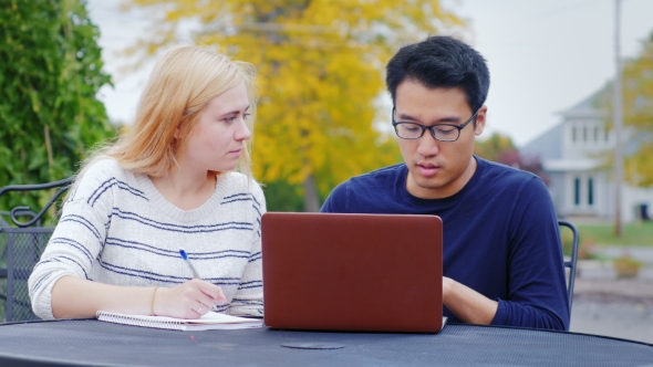 Two Business Man - Asian Man and Caucasian Woman Communicate, Work with a Laptop. The Summer Terrace