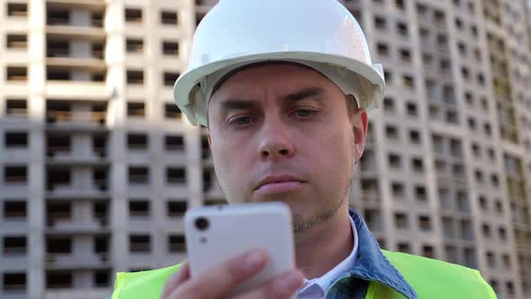 Worker Staff in Protective Helmet Using Smartphone at Construction Site