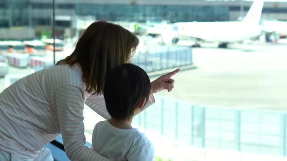 lAsian Mother And Her Son Looking Through Window At Airport