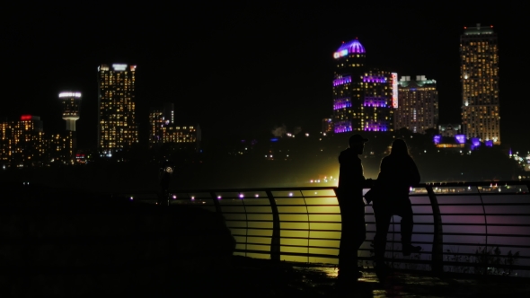 Silhouettes of Men and Women Against the Background of Skyscrapers in a Night City. Communicate