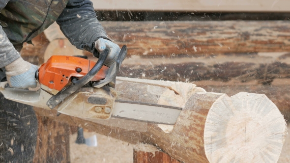 Construction Worker Cuts Wood Chainsaw for Future Home. Protective Mask and Headphones on the Head