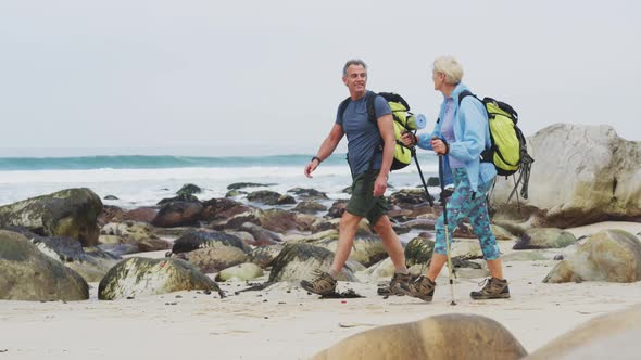 Senior hiker couple with backpack and hiking poles talking to each other and walking while hiking