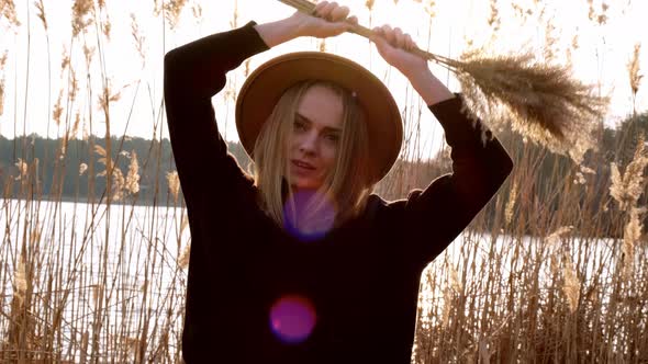 Caucasian Blonde Woman Waving Pampas Grass with Beige Hat in Black Sweater in the Countryside