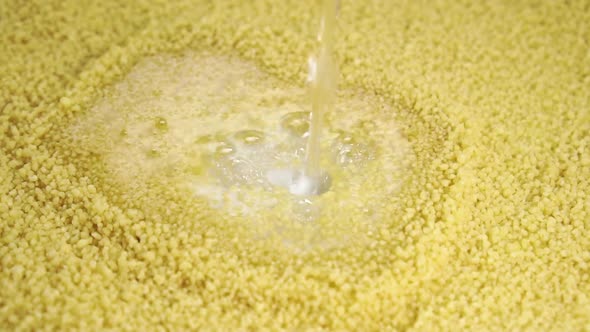 Cooking couscous. Pouring water into a pile of yellow dry grains in slow motion