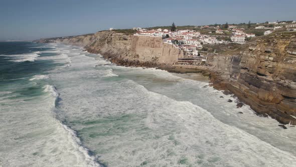 Town of Azenhas Do Mar on high stone cliffside with sea waves hit coastline, aerial drone view