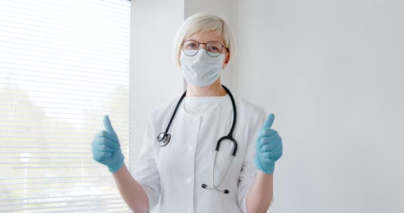 Mature woman doctor receive good results show thumb-up, wear face mask and gloves.