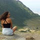 A cinematic view from behind of a young woman sitting on a cliff face looking out over the mountains - VideoHive Item for Sale