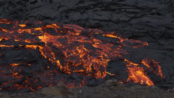 Glowing stream of incandescent lava flowing in desolated landscape